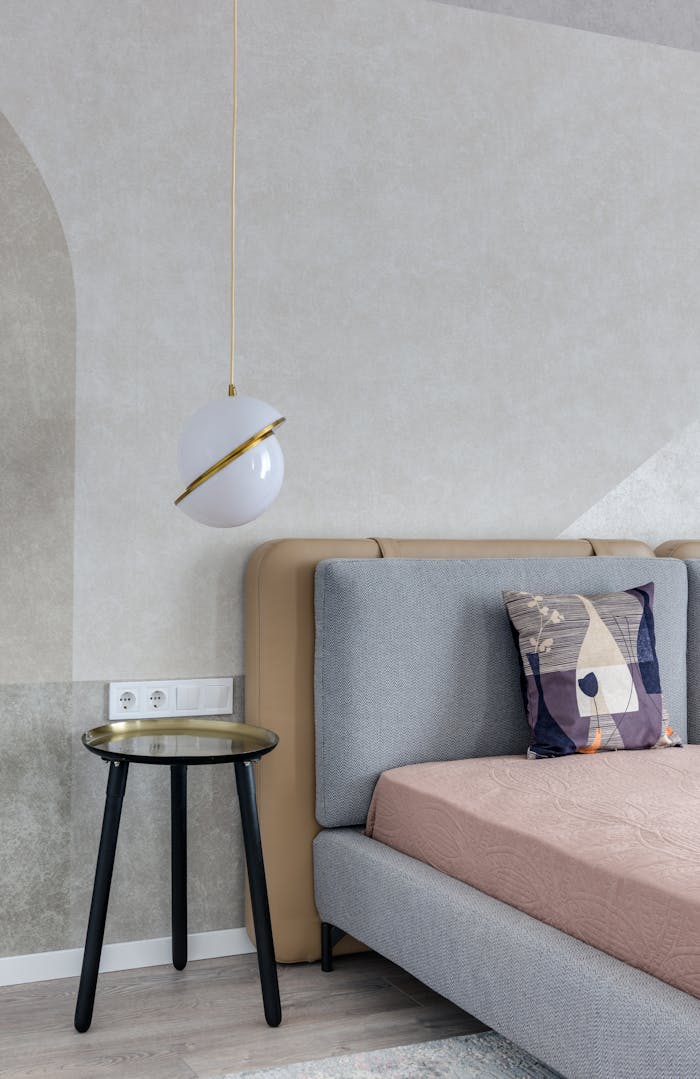 services-05 Comfortable bed with colorful pillow near bedside table under lamp with creative design